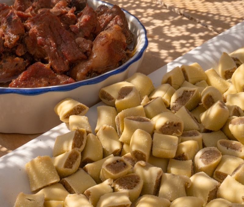 Mezze maniche ripiene accanto a una terrina di carne brasata