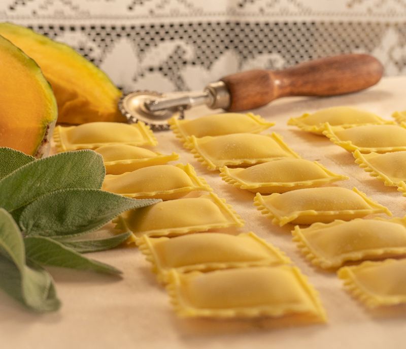 Tortelli quadrati di zucca con la rotella, una fetta di zucca e la salvia